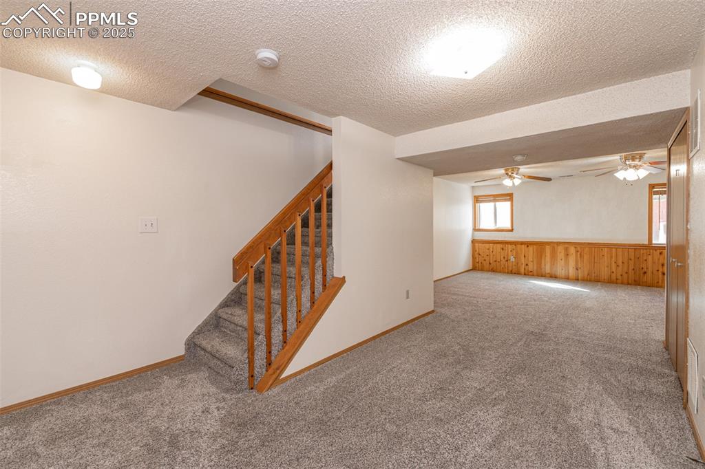 Image 19 of 31: Spare room featuring carpet, a textured ceiling, a ceiling fan, stairs, and