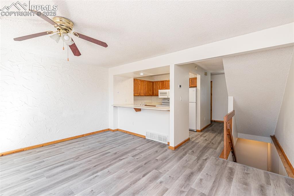 Image 8 of 31: Unfurnished living room with a textured wall, light wood-style flooring, ce