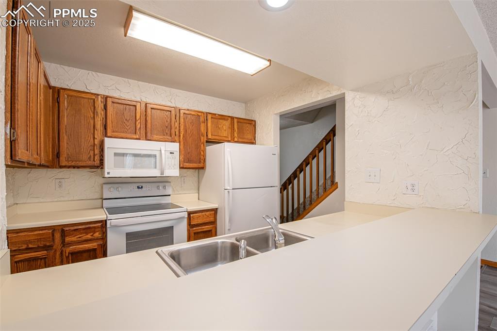 Image 9 of 31: Kitchen featuring brown cabinetry, a textured wall, light countertops, and
