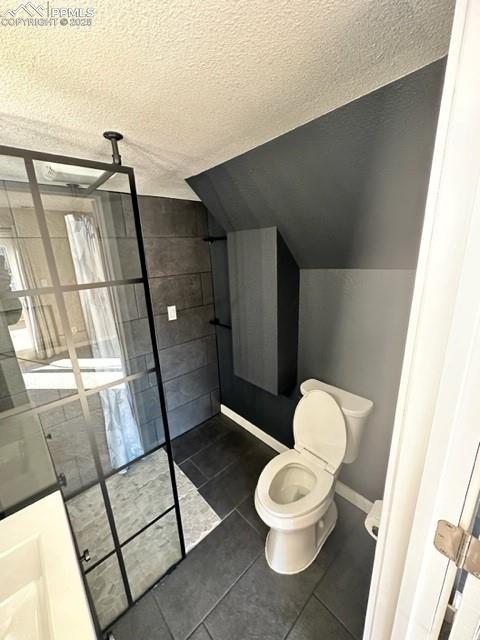 Image 10 of 24: Bathroom with dark tile patterned flooring, a textured ceiling, and lofted 