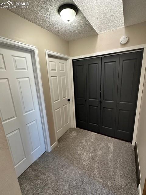 Image 17 of 24: Unfurnished bedroom with a textured ceiling, dark colored carpet, and a clo