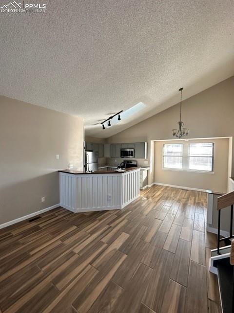 Image 6 of 24: Unfurnished living room with wood finish floors, lofted ceiling, track ligh