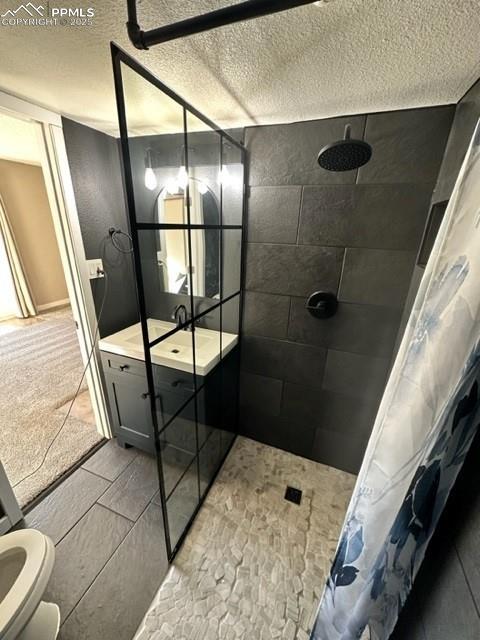 Image 9 of 24: Bathroom featuring a textured ceiling, tiled shower, and vanity