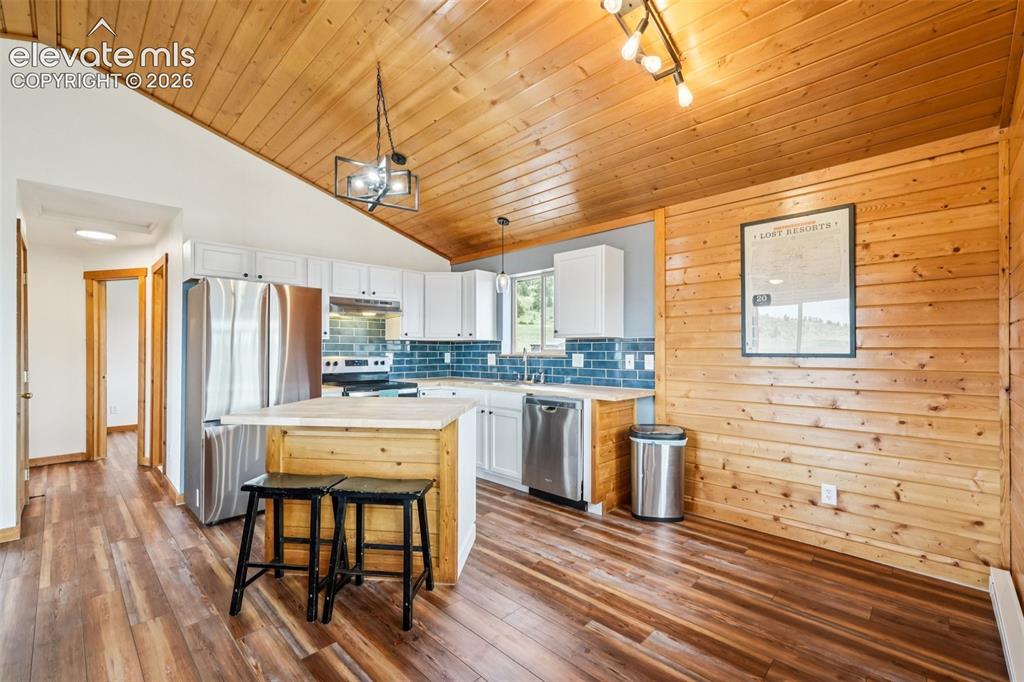 Image 15 of 33: Kitchen featuring a vaulted wood-paneled ceiling, white cabinetry, stainles
