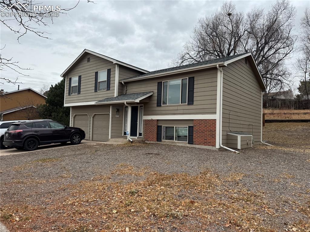 Caption: View of front of house featuring brick siding, gravel driveway, and a garage
