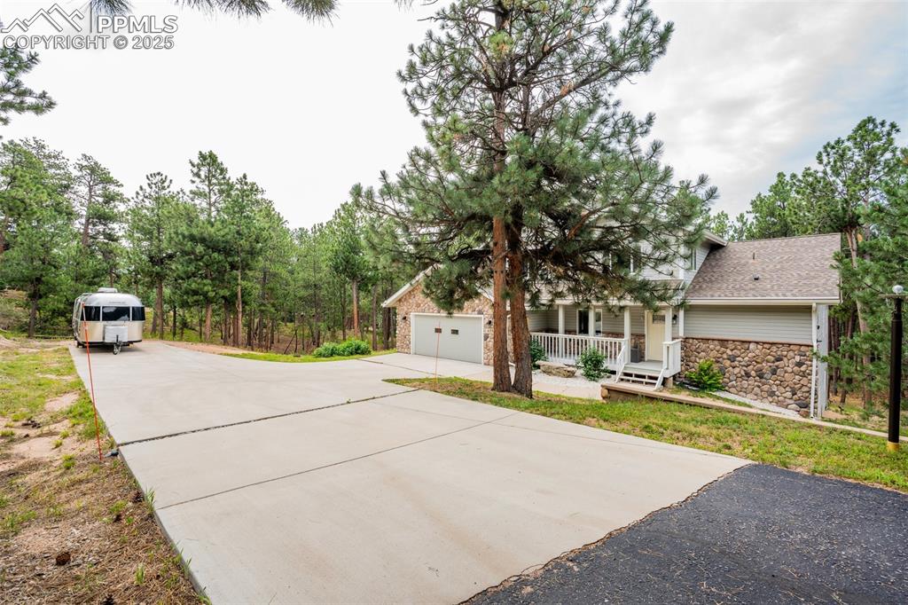 Image 2 of 50: View of front facade featuring a porch, driveway, stone siding, roof with s