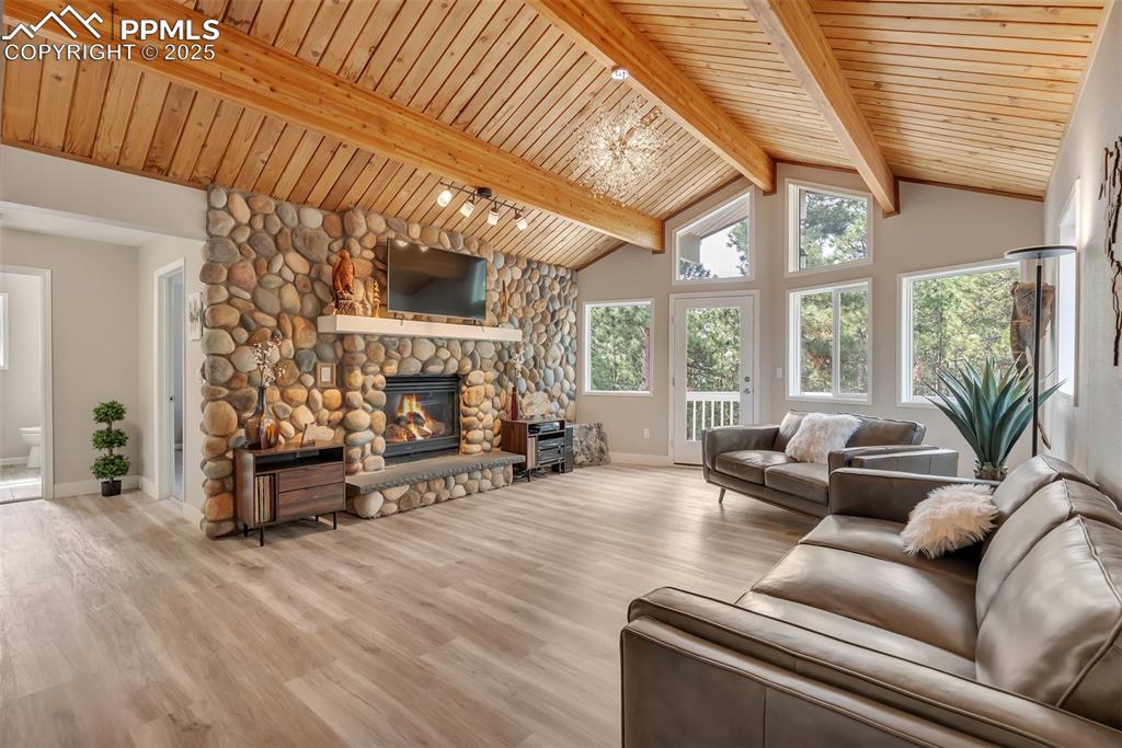 Image 25 of 50: Living room with a chandelier, wood finished floors, a stone fireplace, a w