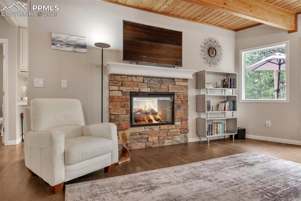 Image 6 of 50: Sitting room with a wooden ceiling with exposed beams, a stone fireplace, a