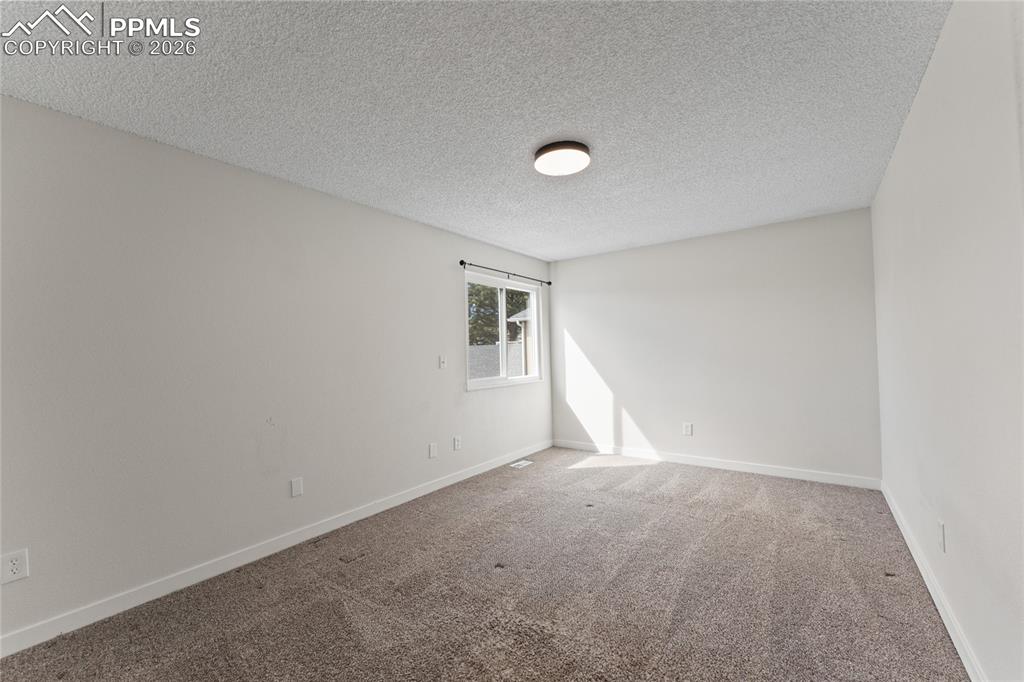 Image 11 of 16: Carpeted empty room with a textured ceiling and baseboards