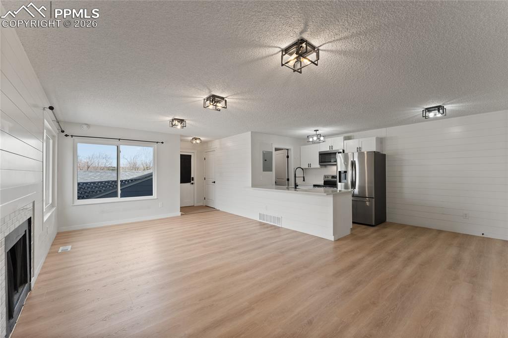 Image 6 of 16: Unfurnished living room with light wood-type flooring, a fireplace, a textu