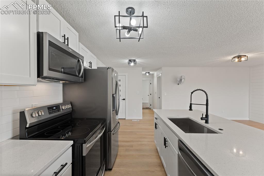 Image 8 of 16: Kitchen with stainless steel appliances, white cabinets, light wood-style f