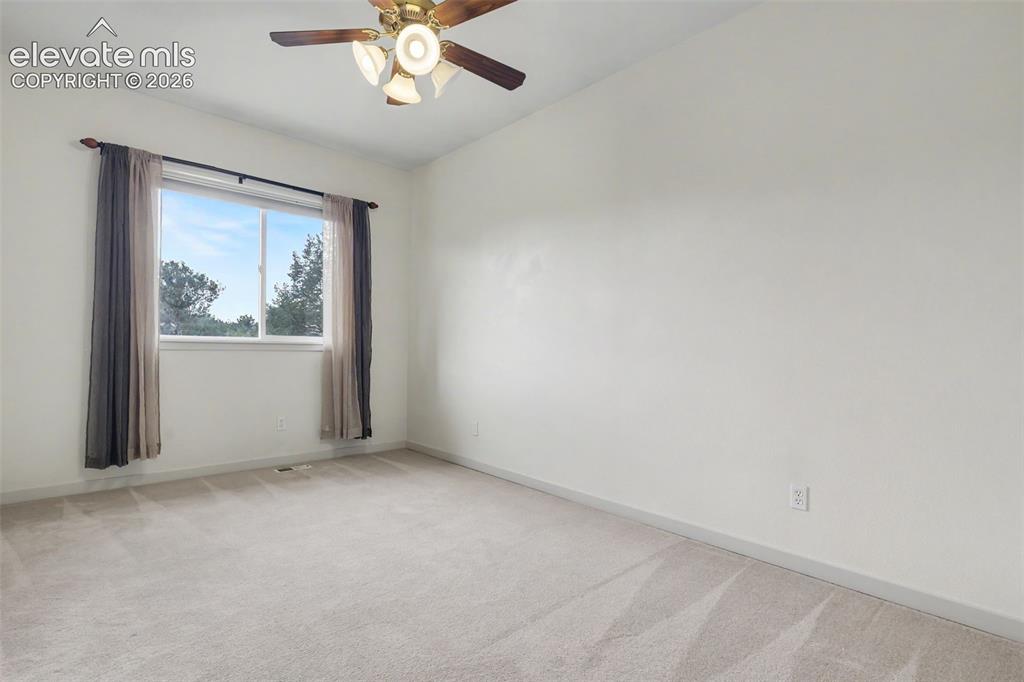 Image 27 of 47: Spacious room featuring neutral carpeting, a large window, and a ceiling fa