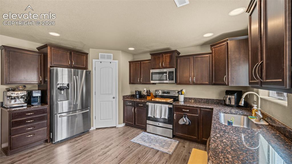 Image 13 of 41: Kitchen featuring wood-finish flooring, dark wood cabinetry, stainless stee