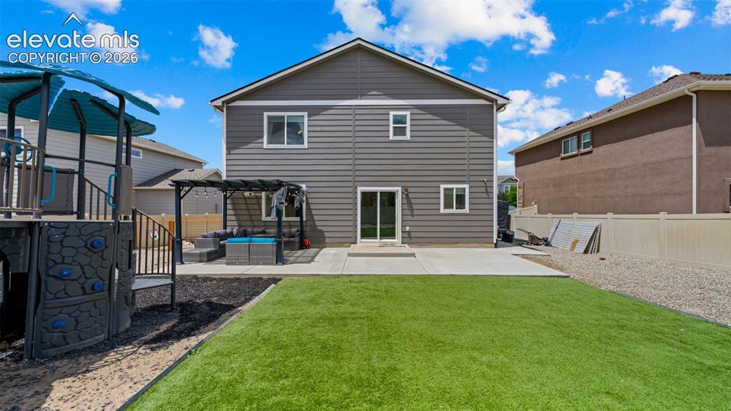 Image 16 of 41: Rear exterior featuring gray siding, a concrete patio, and an artificial tu