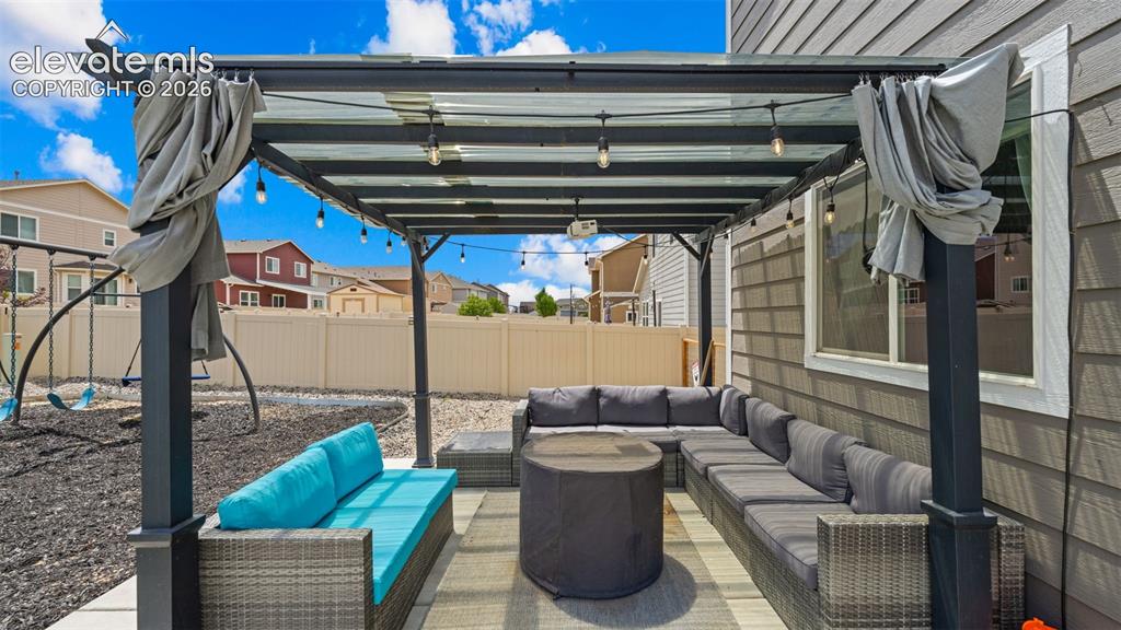 Image 18 of 41: Outdoor patio featuring a black metal pergola with string lighting and drap