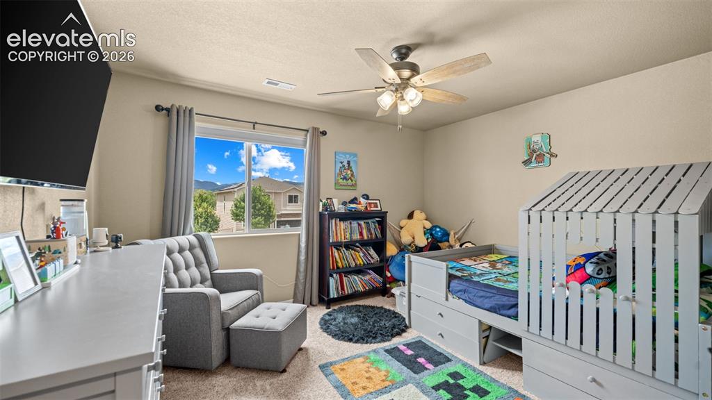 Image 19 of 41: Carpeted room with a ceiling fan light fixture, window with drapes, and a b