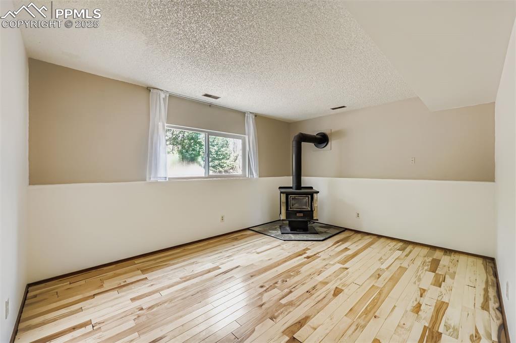 Image 20 of 45: Spare room with a wood stove, light wood-style floors, and a textured ceili