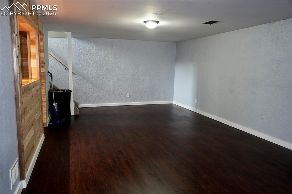 Image 12 of 23: Unfurnished living room featuring a textured wall and dark wood-type floori