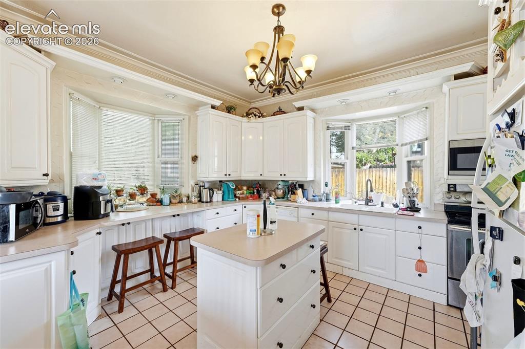 Image 3 of 35: White cabinetry, bay window, center island, tile flooring, and integrated s