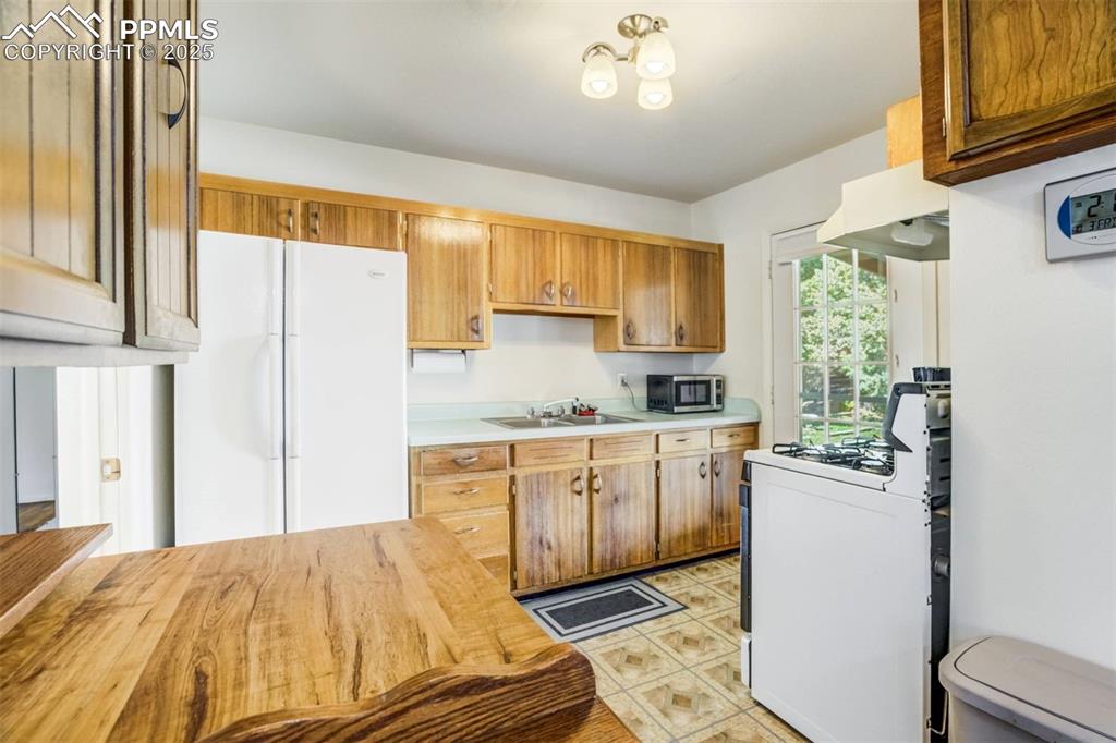 Image 11 of 47: Kitchen with white appliances, brown cabinetry, under cabinet range hood, a
