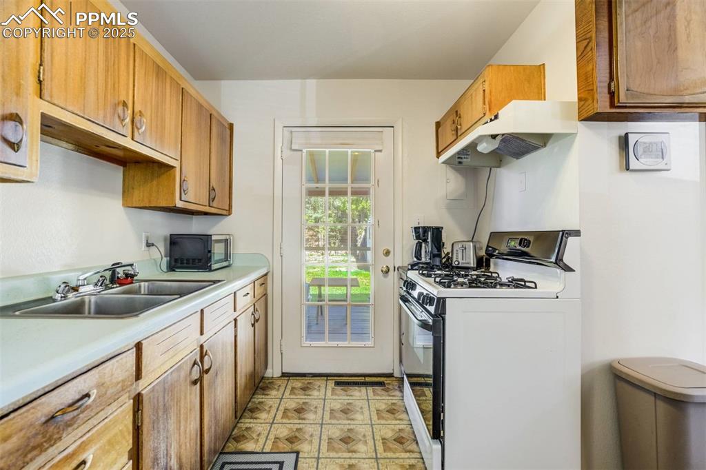 Image 12 of 47: Kitchen featuring gas stove, under cabinet range hood, light countertops, b