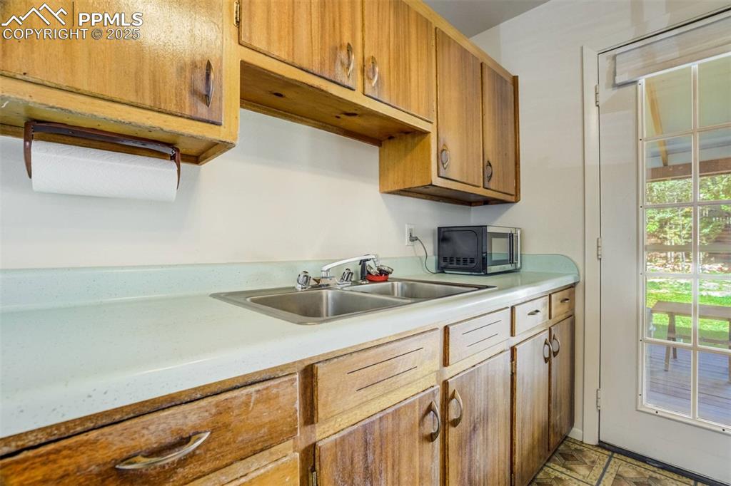 Image 13 of 47: Kitchen with light countertops, brown cabinets, and stainless steel microwa