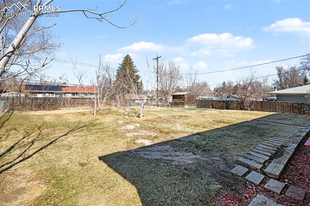 Image 19 of 21: Fenced backyard offers mountain views, mature trees, and space to relax or 