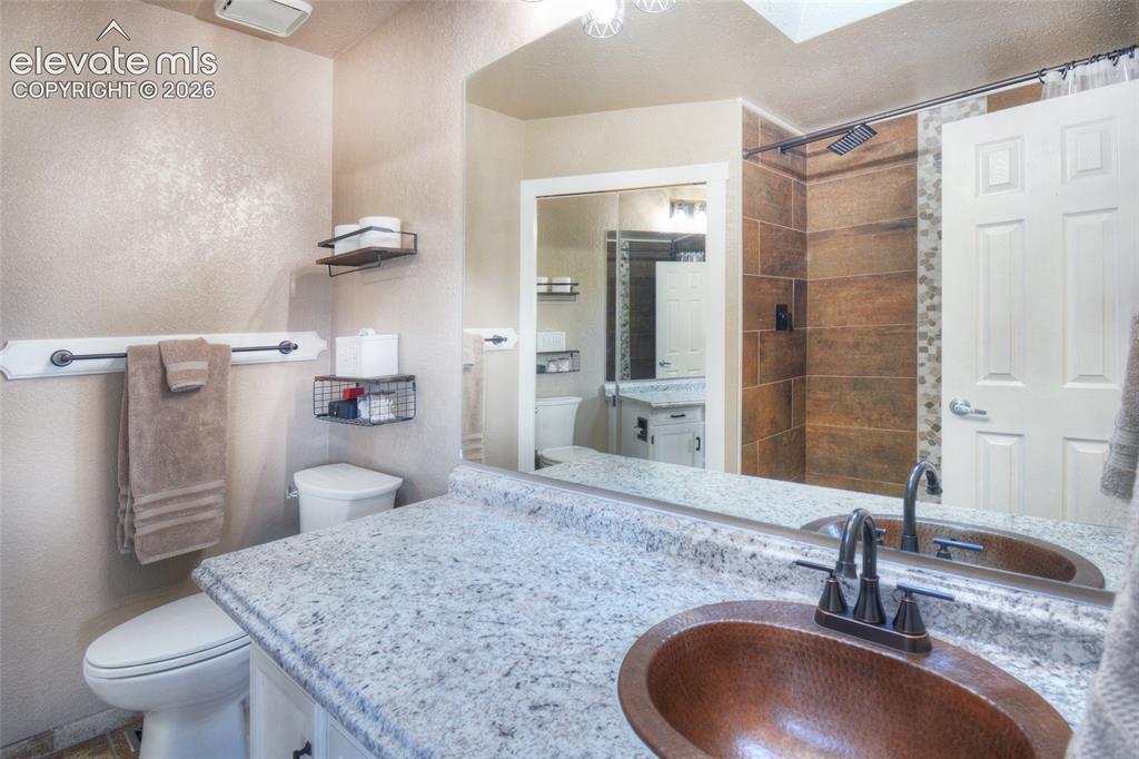 Image 17 of 26: Primary bathroom has a beautiful updated tiled shower, copper sink and walk
