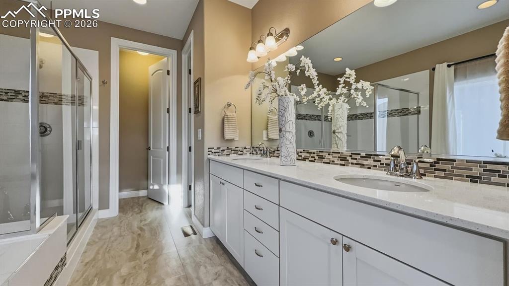 Image 26 of 50: The Primary Bathroom features a dual sink vanity, mirror, jetted tub, and s
