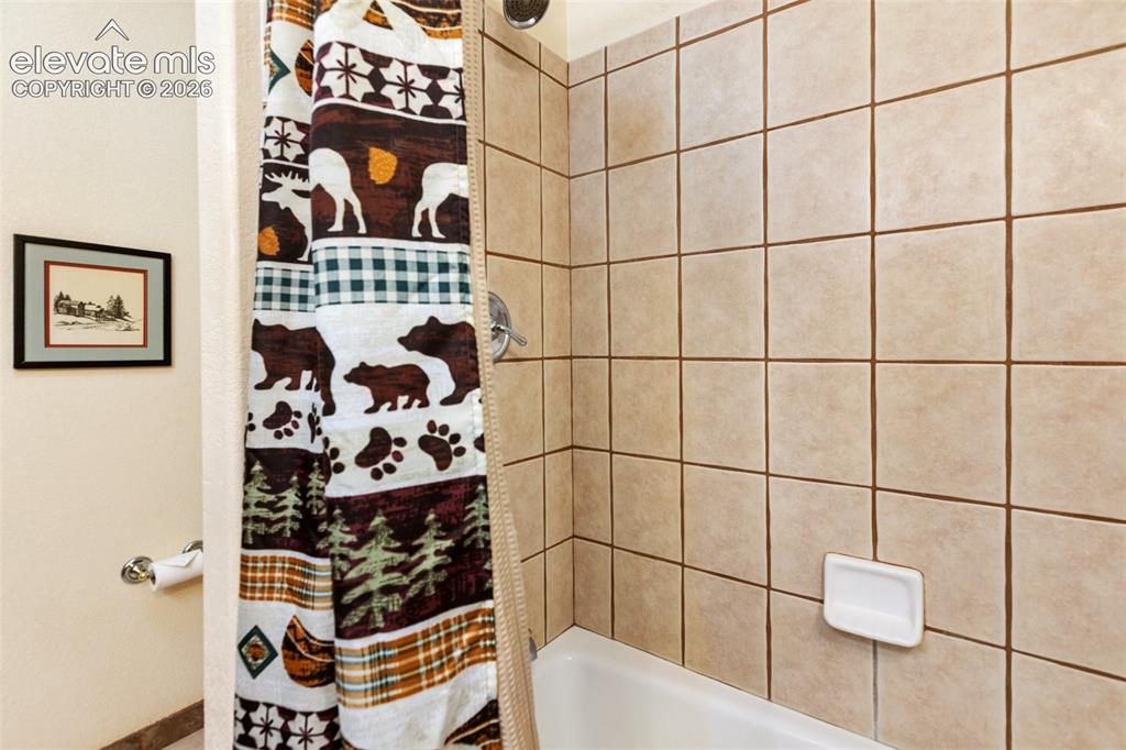 Image 36 of 50: Tub and shower combination with light-toned square wall tiles and a chrome 