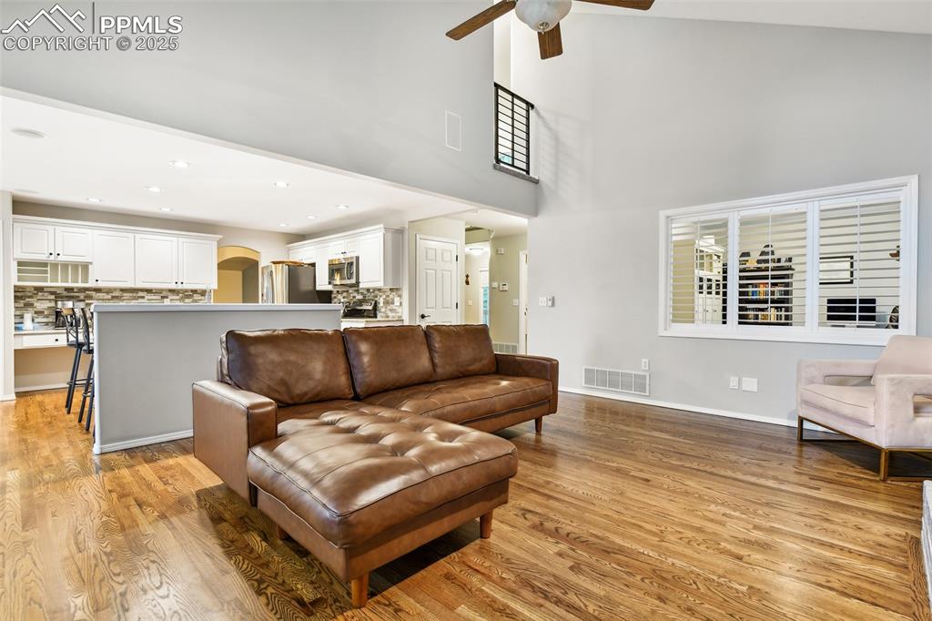 Image 15 of 47: Living area featuring a ceiling fan, a towering ceiling, light wood-style f