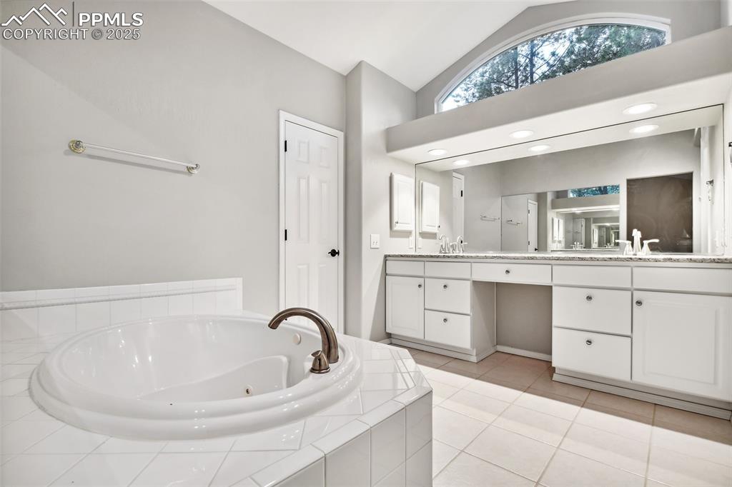 Image 22 of 47: Full bathroom with double vanity, a tub with jets, high vaulted ceiling, an