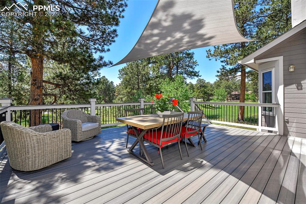 Image 42 of 47: Wooden terrace with outdoor dining area and view of wooded area
