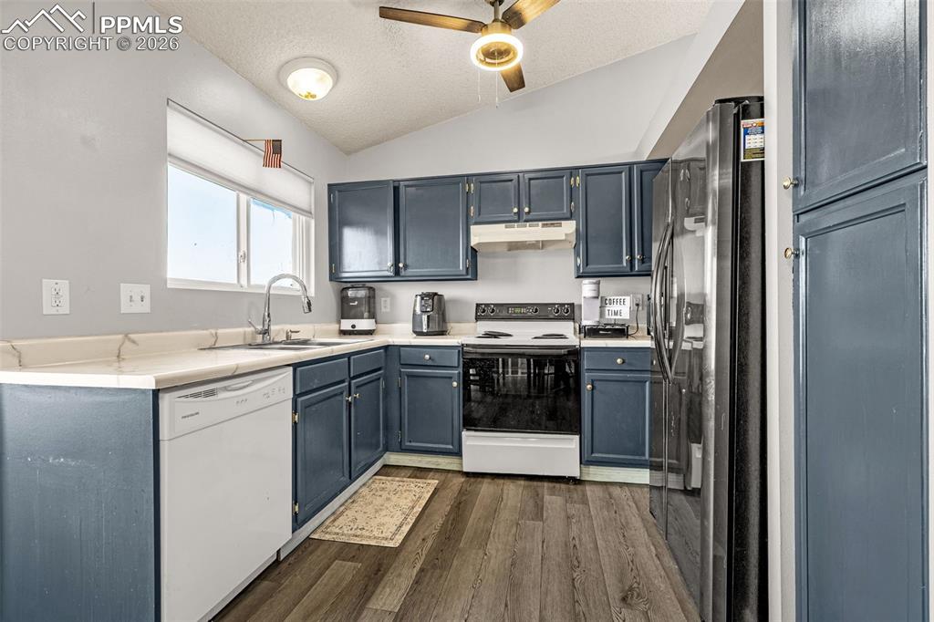 Image 8 of 30: Kitchen with a textured ceiling, white appliances, light countertops, dark 