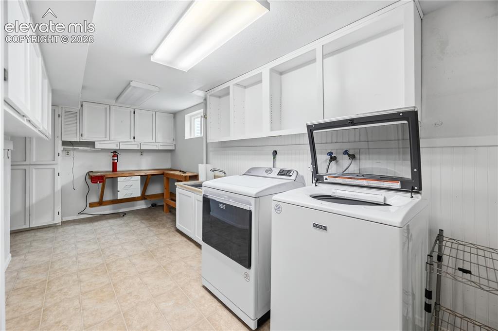 Image 17 of 25: Laundry room featuring abundant white cabinetry, a built-in workbench, wood