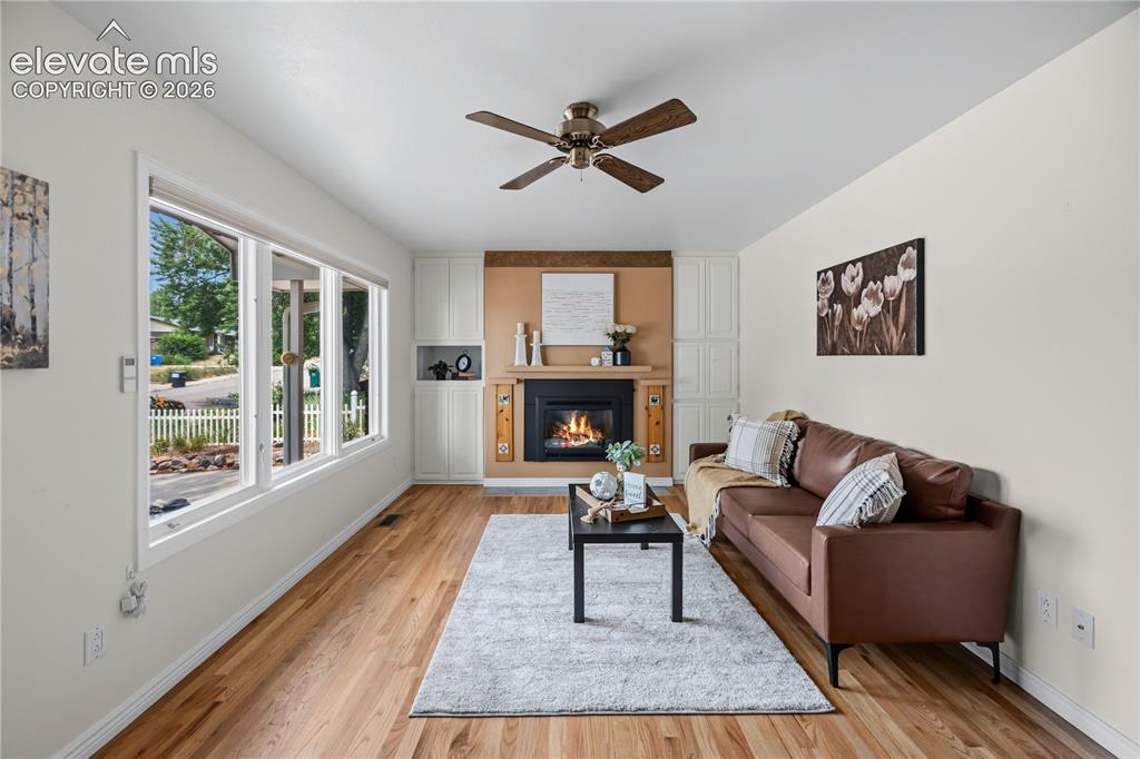 Image 2 of 25: Living area featuring wood-finish flooring, a ceiling fan, and a fireplace 