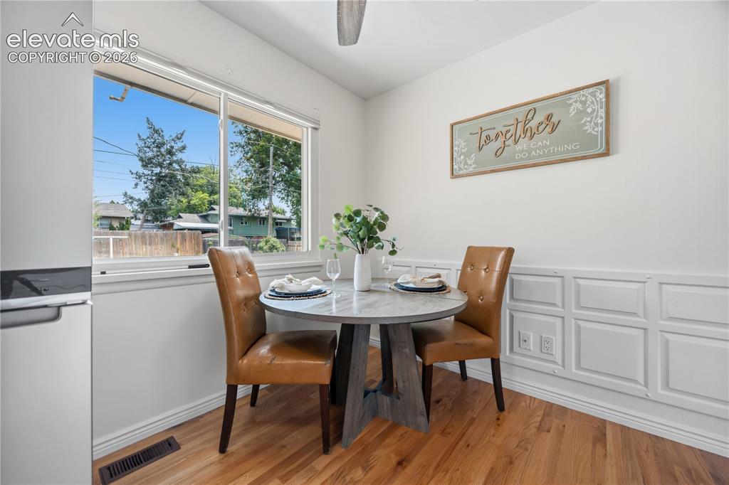 Image 4 of 25: Dining area featuring hardwood flooring, a large window, and white wainscot