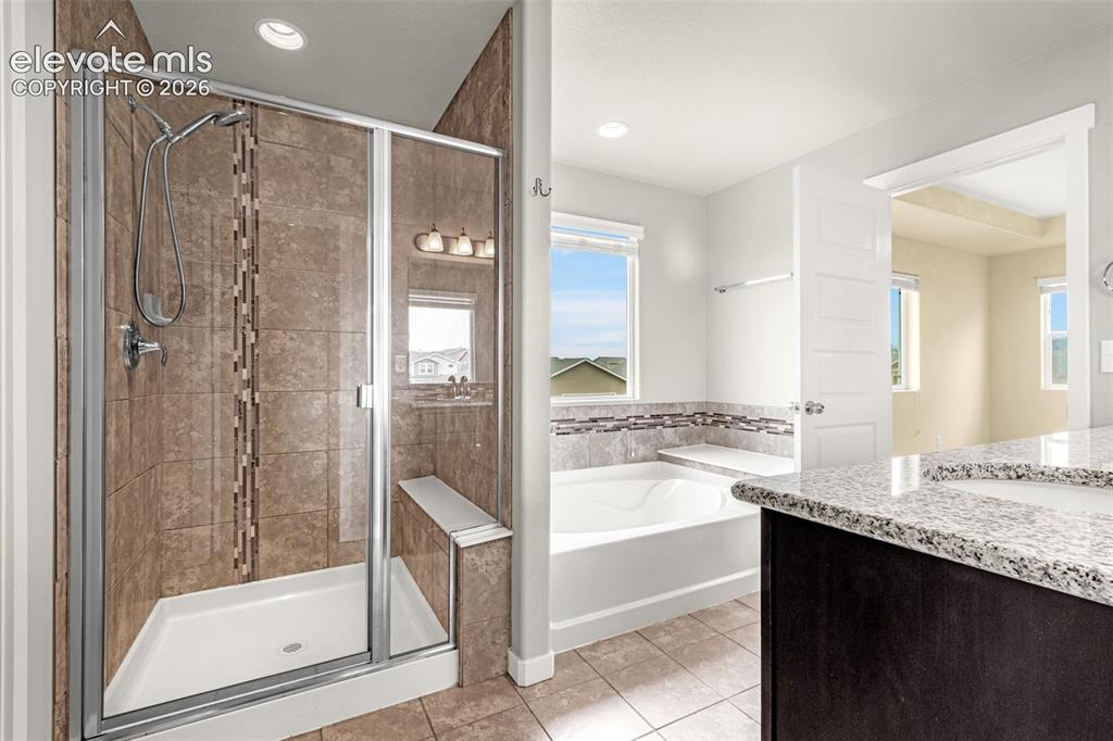 Image 28 of 44: Enclosed shower with a built-in bench, a separate soaking tub, and a dual-s