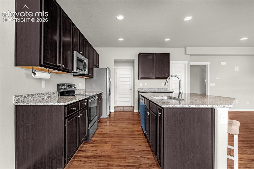 Image 9 of 44: Kitchen featuring wood-finish flooring, dark wood cabinetry, granite counte