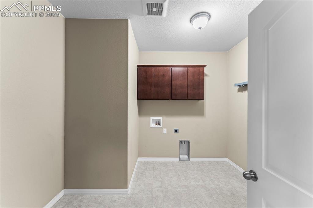 Image 10 of 45: Laundry area featuring a textured ceiling, cabinet space, hookup for an ele