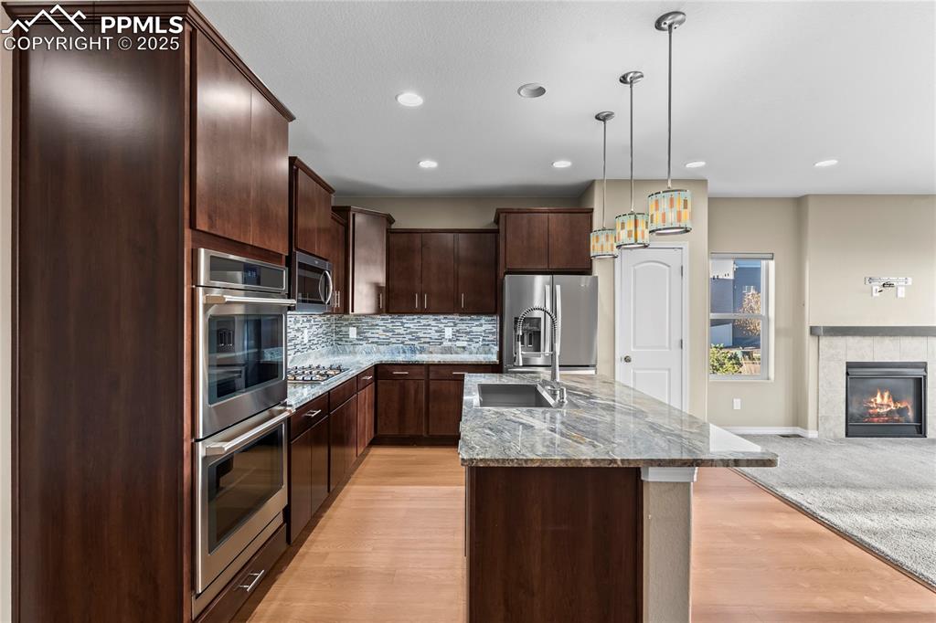 Image 13 of 45: Kitchen featuring dark brown cabinets, light stone counters, a center islan