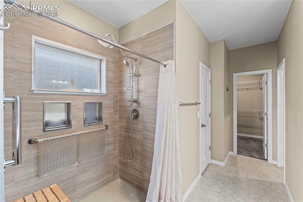 Image 21 of 45: Bathroom with a tile shower, a walk in closet, and light tile patterned flo
