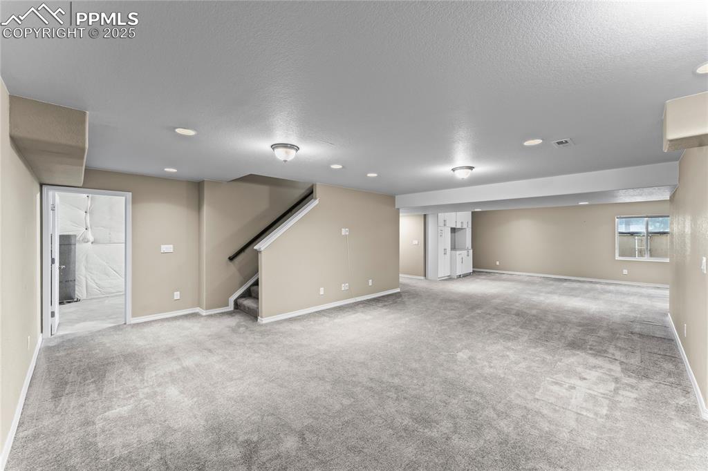 Image 26 of 45: Basement with light colored carpet, stairs, and a textured ceiling