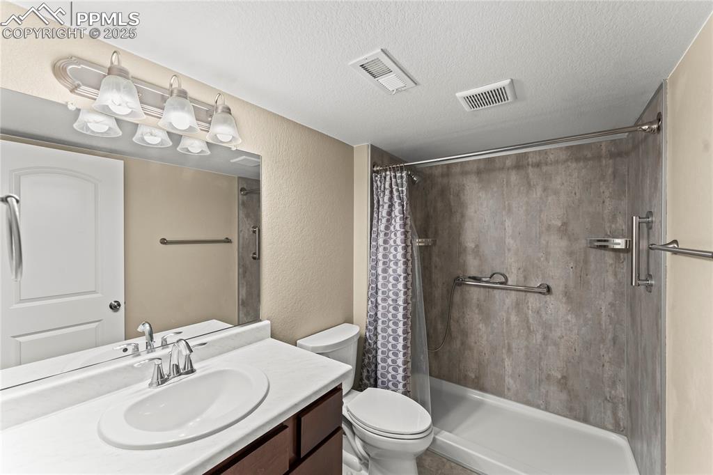 Image 31 of 45: Full bath with a textured wall, vanity, a tile shower, and a textured ceili