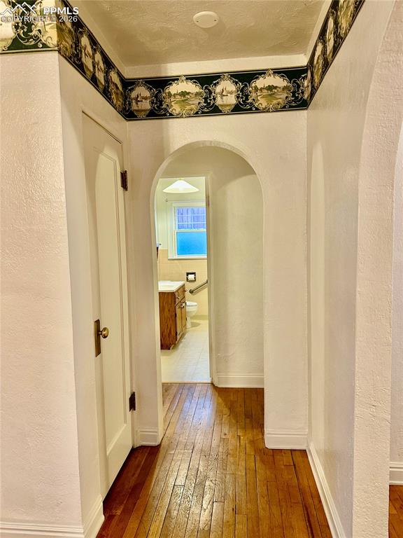 Image 11 of 28: Hallway with a textured wall, dark wood-style floors, and arched walkways