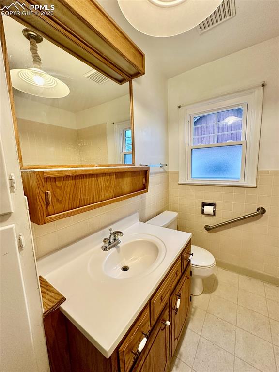 Image 14 of 28: Bathroom with vanity, wainscoting, plenty of natural light, light tile patt
