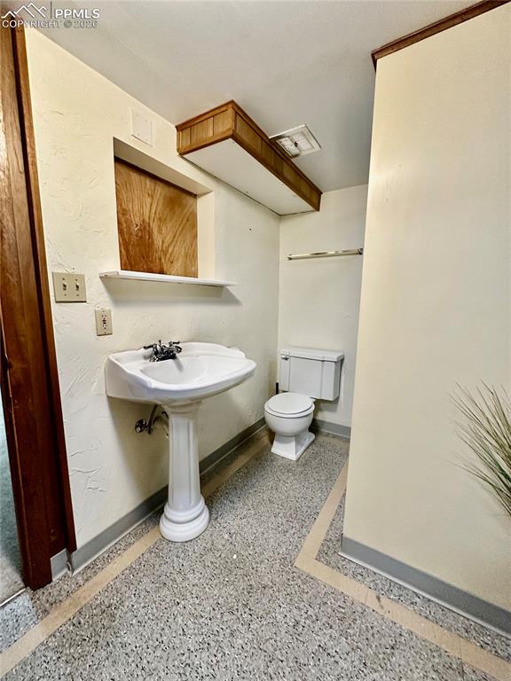 Image 22 of 28: Half bath featuring dark aggregate flooring and a textured wall