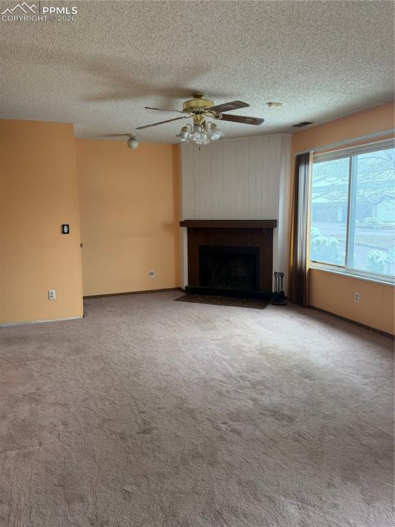 Image 3 of 12: Living area featuring a central fireplace with a wood mantel, a ceiling fan