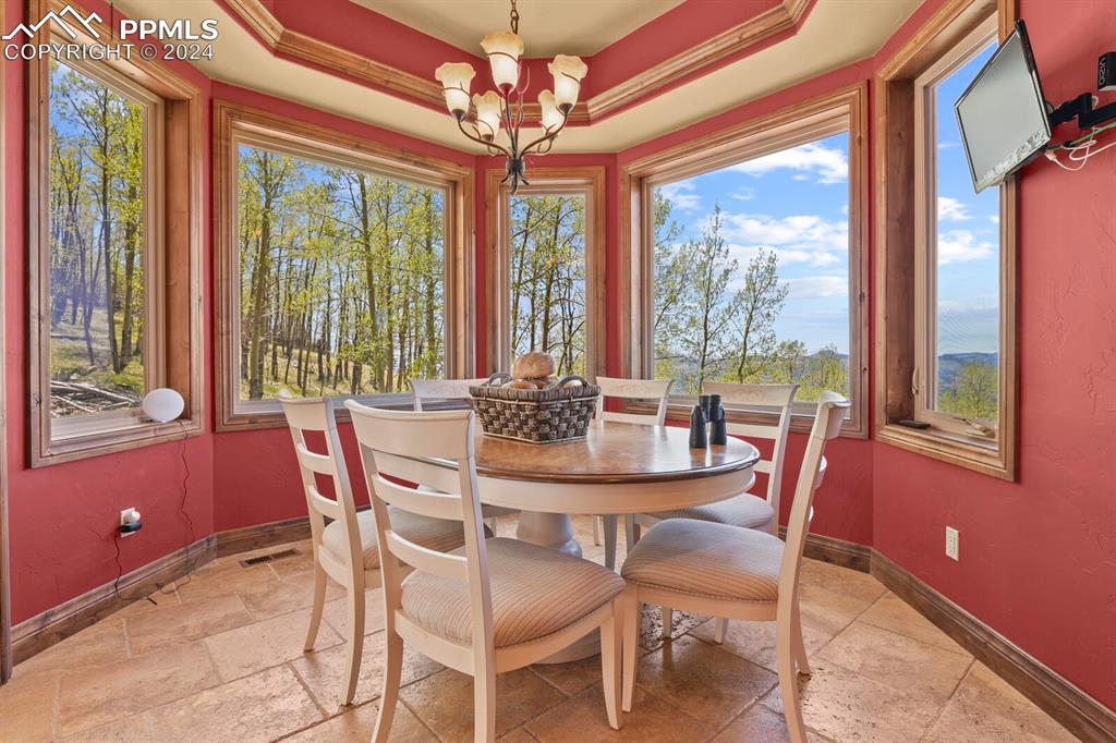 Image 12 of 50: Dining space with a notable chandelier, tile floors, and a raised ceiling