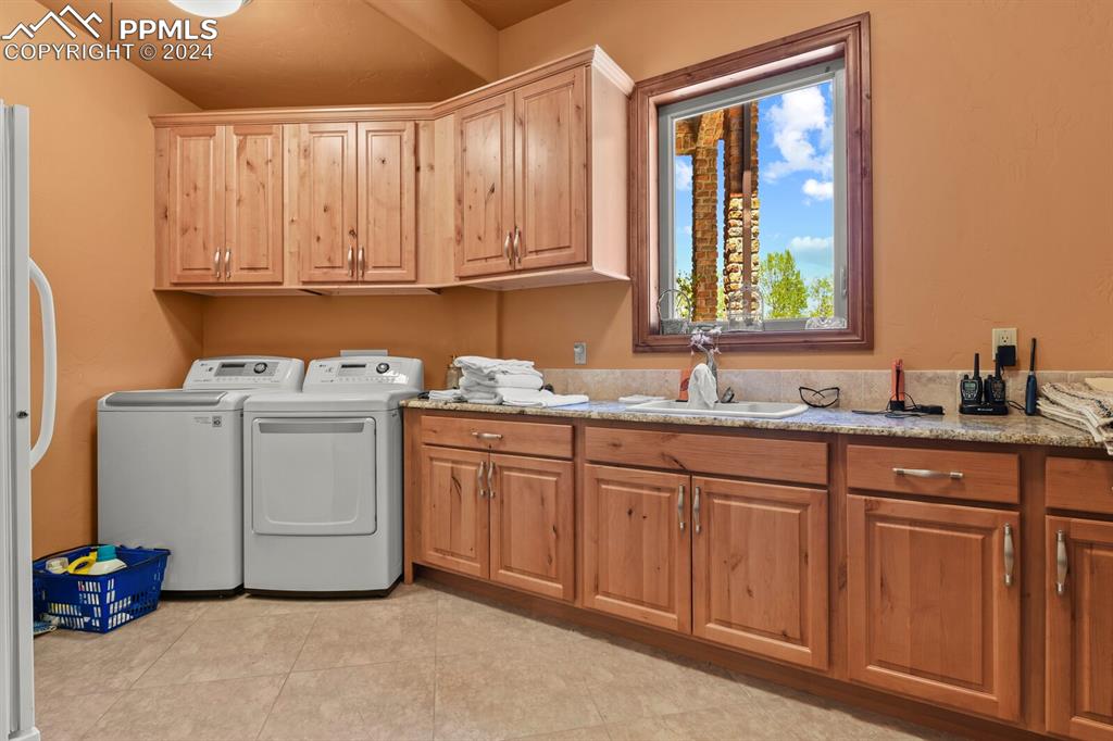 Image 17 of 50: Laundry area with cabinets, sink, light tile floors, and washing machine an